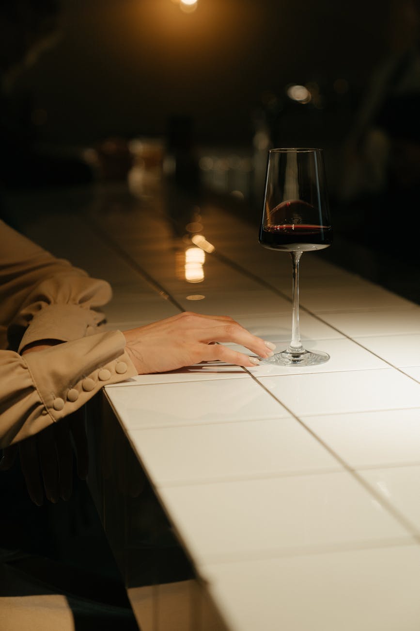 person in brown coat holding clear wine glass