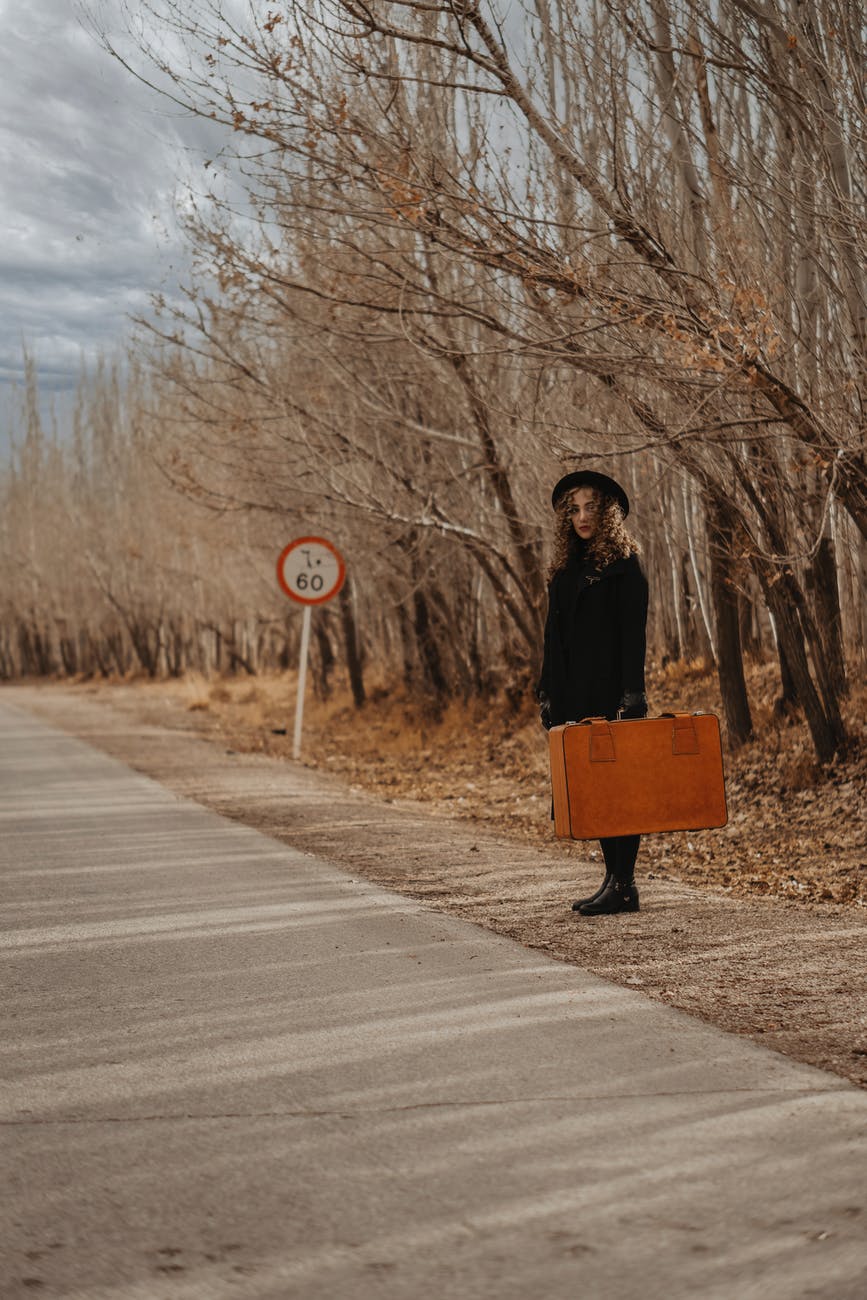 woman with vintage suitcase near asphalt road