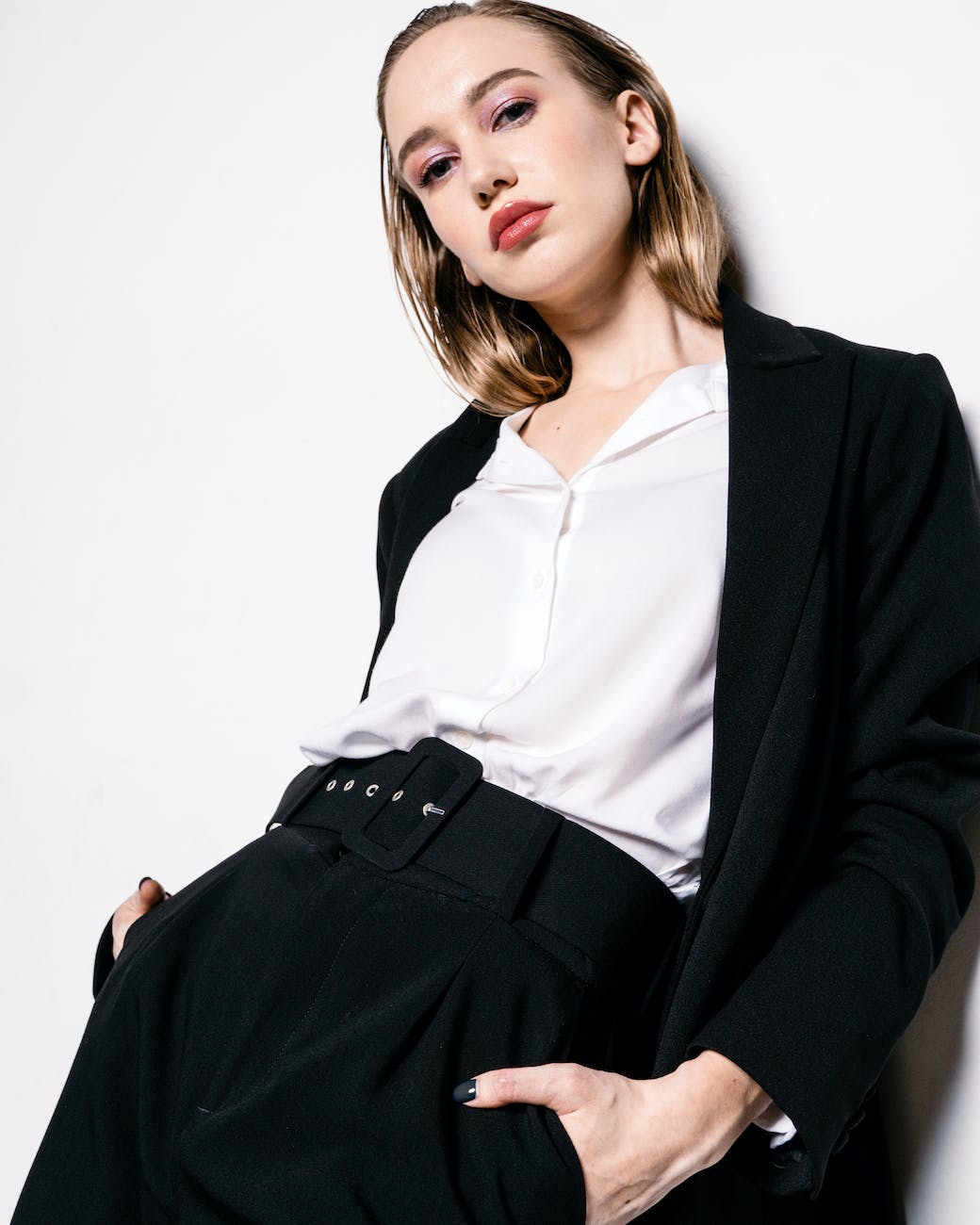 a low angle shot of a woman in black blazer leaning on the wall