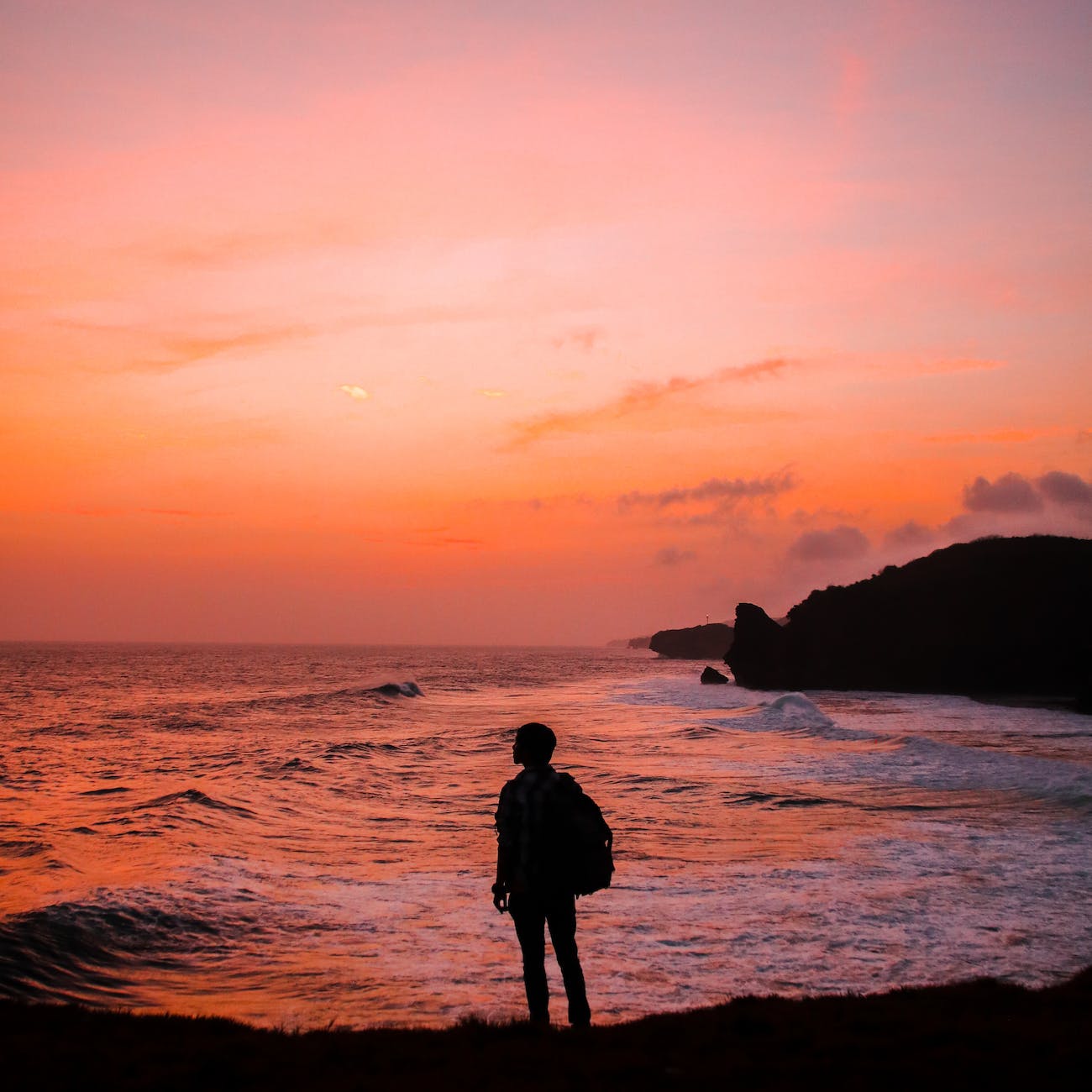 silhouette photo of man with backpack standing in seashore during golden hour